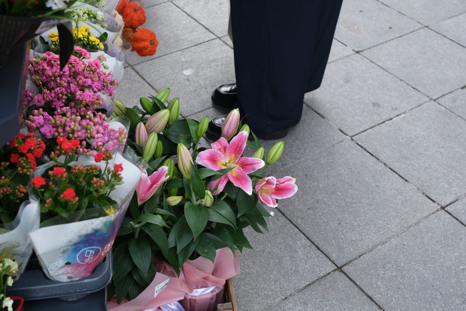A vibrant display of fresh flowers at Barkingside Florist, including large pink lilies with white streaks and prominent green leaves, arranged in a bouquet wrapped in pastel pink paper. Surrounding th